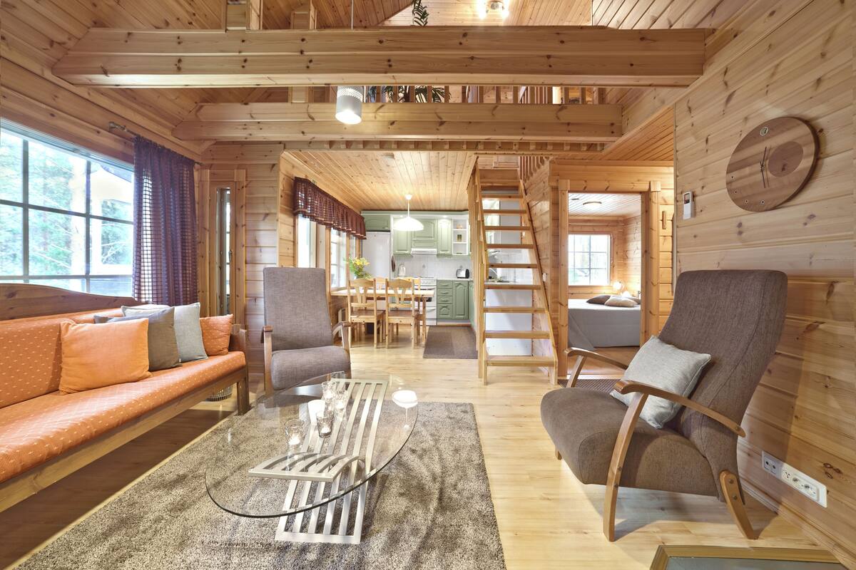 L’intérieur d’un chalet en bois comprend un canapé, des fauteuils, un coin repas, une cuisine et une échelle.