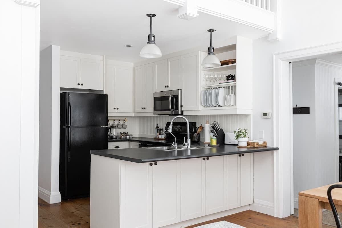 A kitchen with white cabinets, a black refrigerator, a microwave, and a sink.