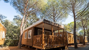 A wooden cabin with a porch, surrounded by trees. - Mobilhome im Ferienpark mit Grosser Poolanlage (Castiglione della Pescaia)