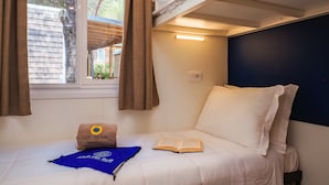 A bunk bed with a window, a pillow with a logo, a book, and a blue towel. - Mobilhome im Ferienpark mit Grosser Poolanlage (Castiglione della Pescaia)