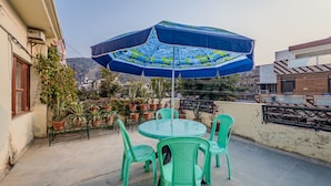 Un patio en la azotea con una mesa redonda, sillas, un paraguas y plantas en macetas.