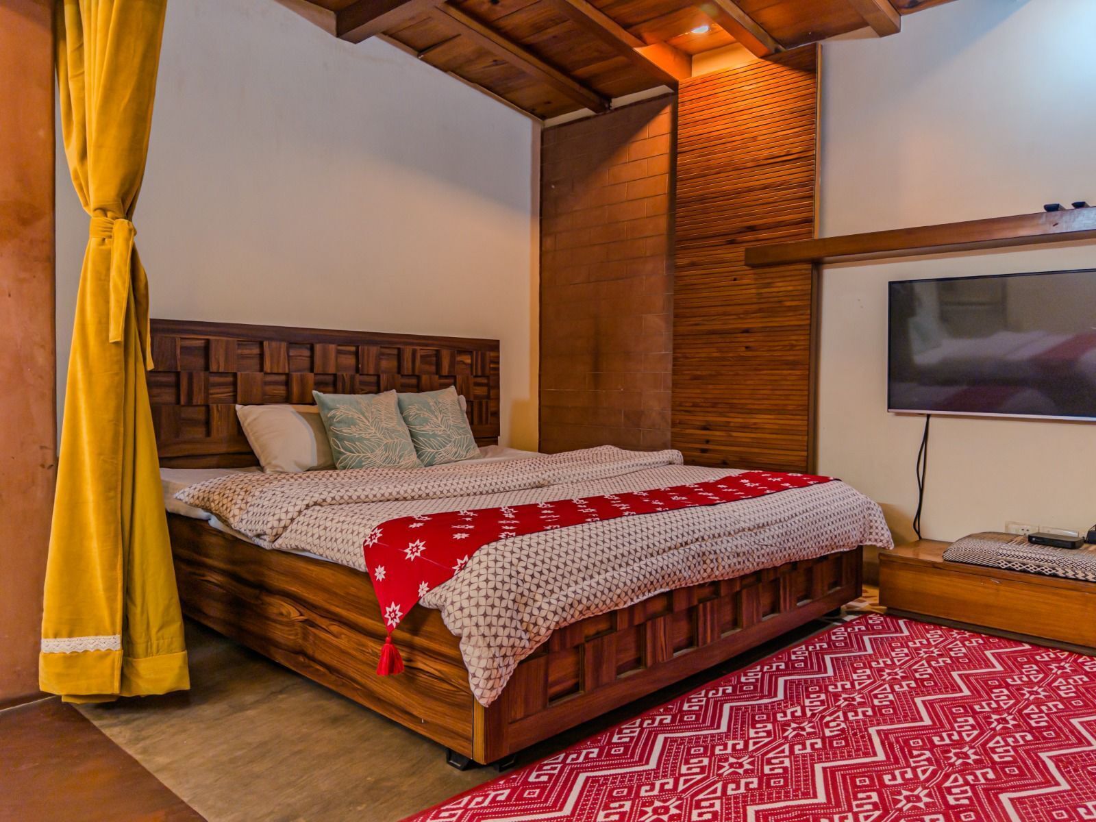 Une chambre à coucher avec un lit en bois, une télévision et un tapis à motifs.