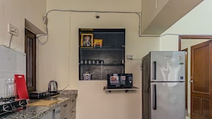 Una cocina compacta con refrigerador, microondas y una repadera con frascos.