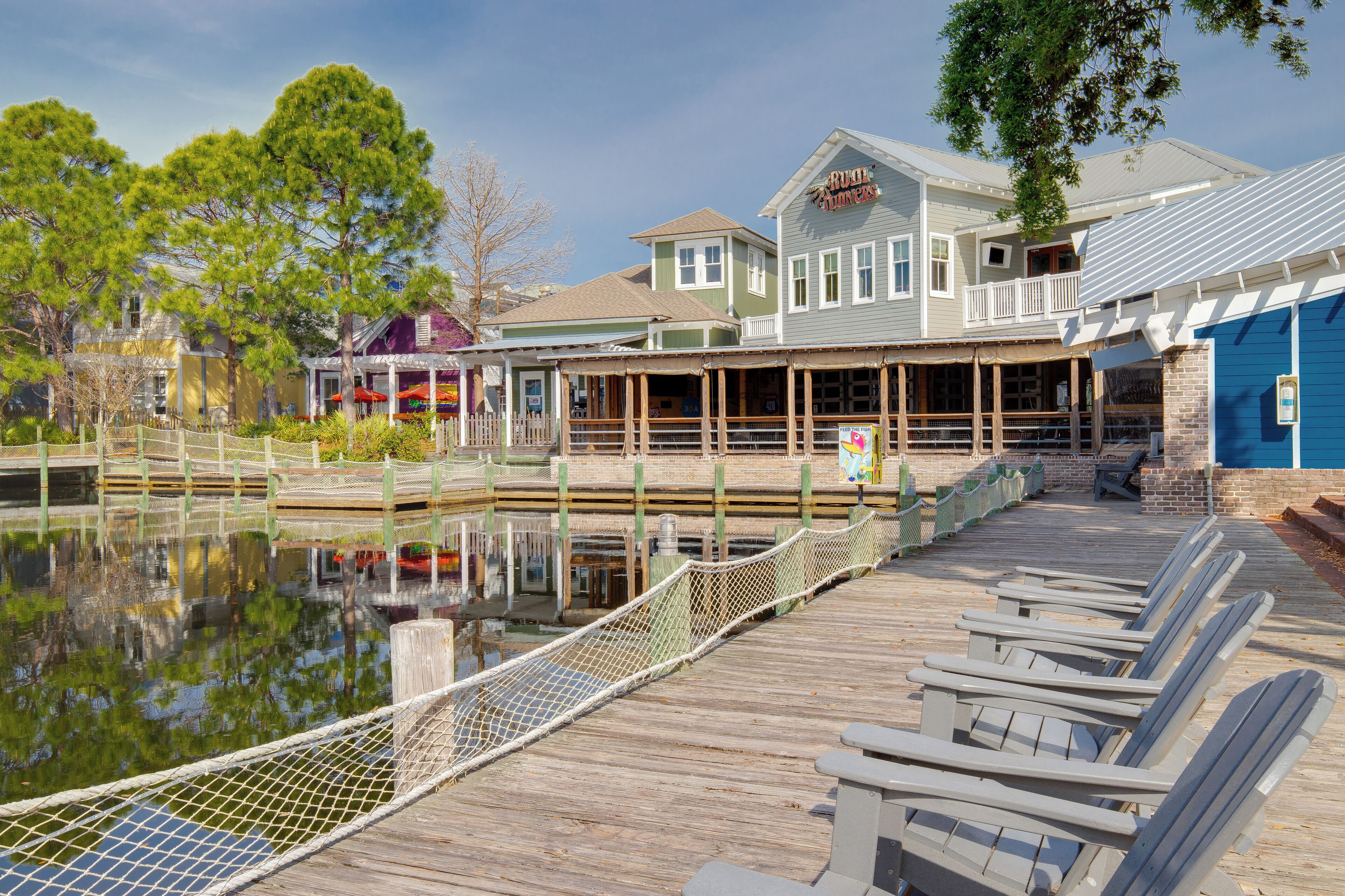 A wooden pier with chairs, a building labeled "Riviera Hotel," and a reflection in the water.