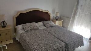 Et soveværelse med en dobbeltseng, to sengeborde, en lampe på hvert bord, en radiator og et vindue med gardiner.