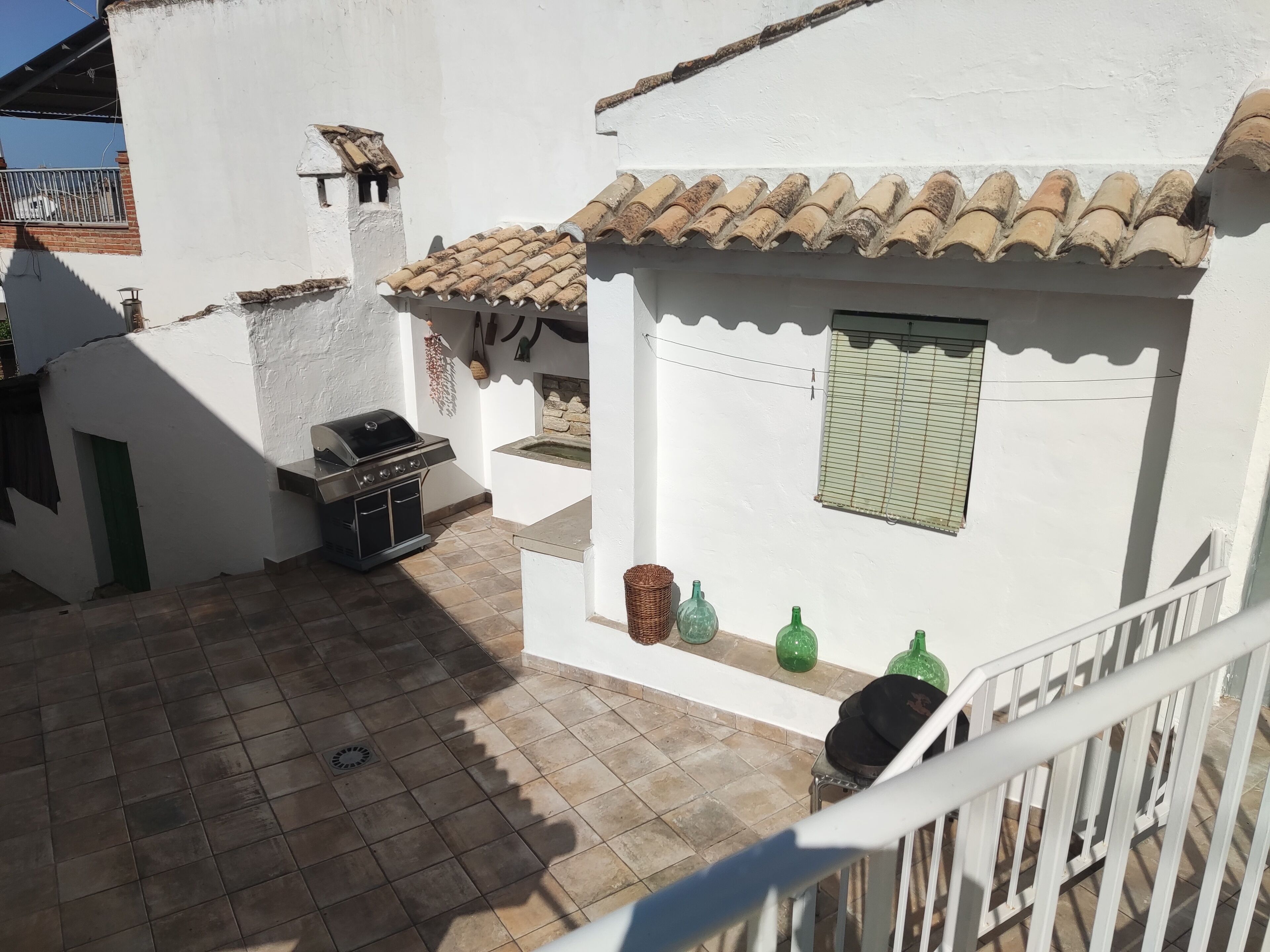 Un bâtiment blanc avec un toit recouvert de tuiles, un barbecue et une petite fenêtre avec des volets.