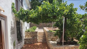 En stentrappe fører op til en bygning med hvide facader og en pergola dækket af slyngplanter.