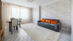 A spacious living room with a grey sofa, a dining table with chairs, and a patterned rug.