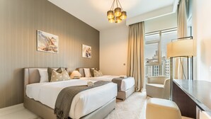 Une chambre d’hôtel avec un grand lit, un lit plus petit, un bureau et une chaise. Il y a deux tableaux au mur et la fenêtre offre une vue sur la ville.