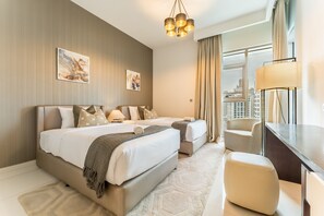 A hotel room with a large bed, a smaller bed, a desk, and a chair. There are two paintings on the wall and a view of the city through the window. - Stylish 2BR with Burj Khalifa Views, Minutes from Marine Transport Station (Dubai)