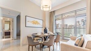 Un espace de salle à manger moderne, avec une table dressée pour quatre personnes, un vase orné de branches et une vue sur la ville à travers de grandes fenêtres.