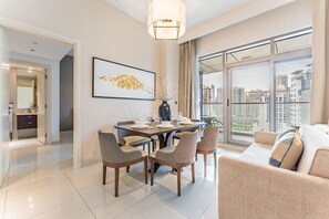 A modern dining area with a table set for four, a vase with branches, and a city view through large windows. - Stylish 2BR with Burj Khalifa Views, Minutes from Marine Transport Station (Dubai)