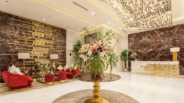 Un hall d’entrée moderne avec un sol en marbre, des canapés rouges, une table ronde centrale et des plantes décoratives.