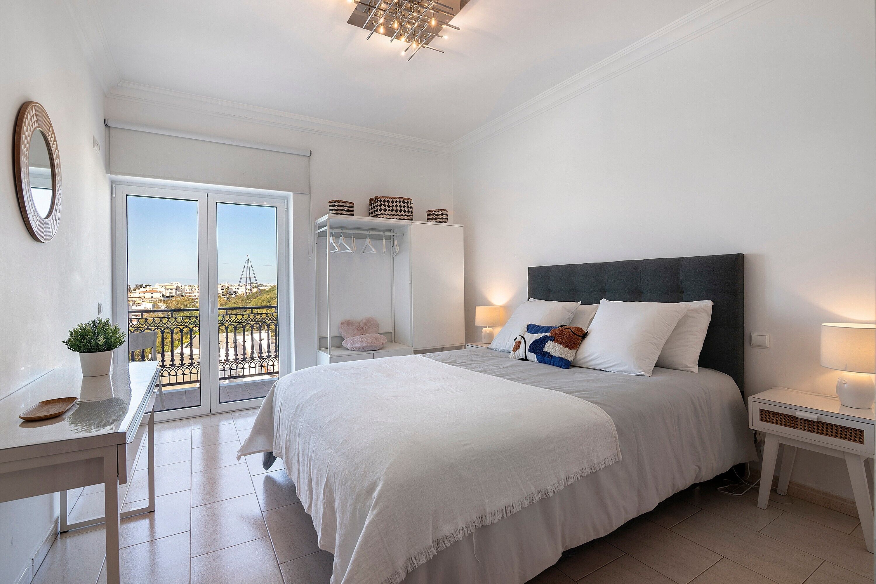 Une chambre à coucher comprenant un lit, des tables de chevet, un miroir, une fenêtre avec vue et un balcon.
