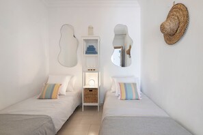 A minimalist room with two beds, a white wardrobe, a mirror, and a woven wall decoration. - Sunny Paradise – Ocean View Holiday Home in Albufeira for 6 Guests (Albufeira)