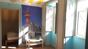 A room with a bed, a desk, a stone wall mural, and a window with a view of a lighthouse. - Meeting Hostel (Figueira da Foz)