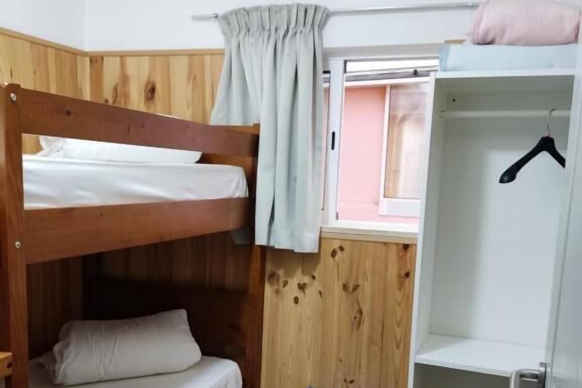 Habitación con literas, ventana, una pequeña estantería azul y un armario con un gancho.