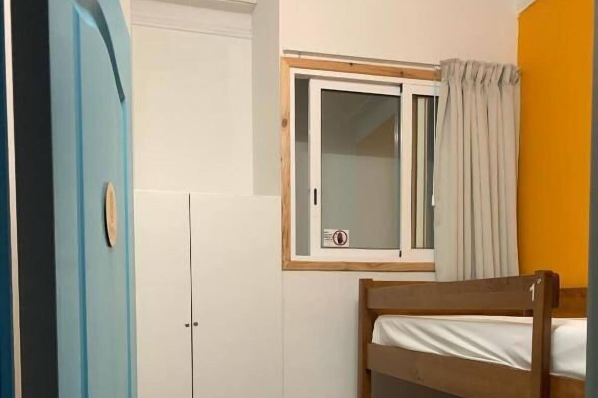 Una habitación con una cama litera, un armario, una ventana con cortinas y una puerta.