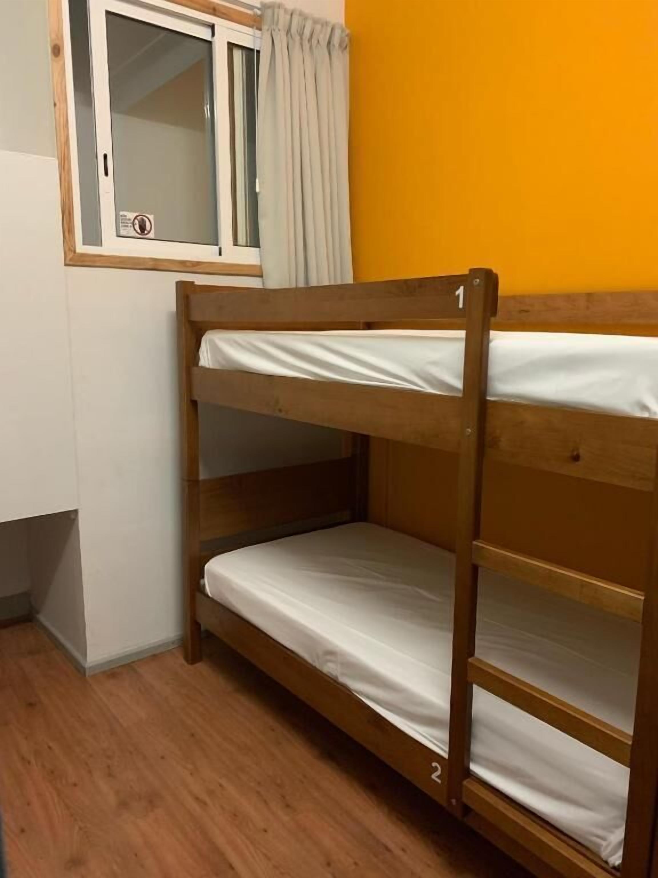 Ein Stockbett mit Fenster und Vorhängen, Holzboden und eine gelbe Wand.