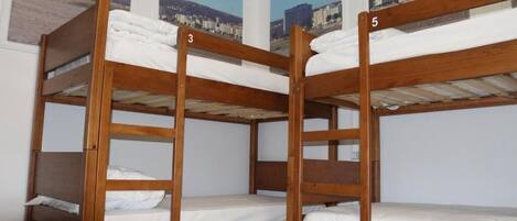 A set of bunk beds with numbers 3 to 6, white bedding, and a cityscape view through the windows.