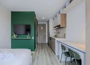 A compact hotel room with a bed, a small kitchenette, a TV, and a green wall. - NOK Stylish 1BR in Chapinero Bogota (Bogotá)