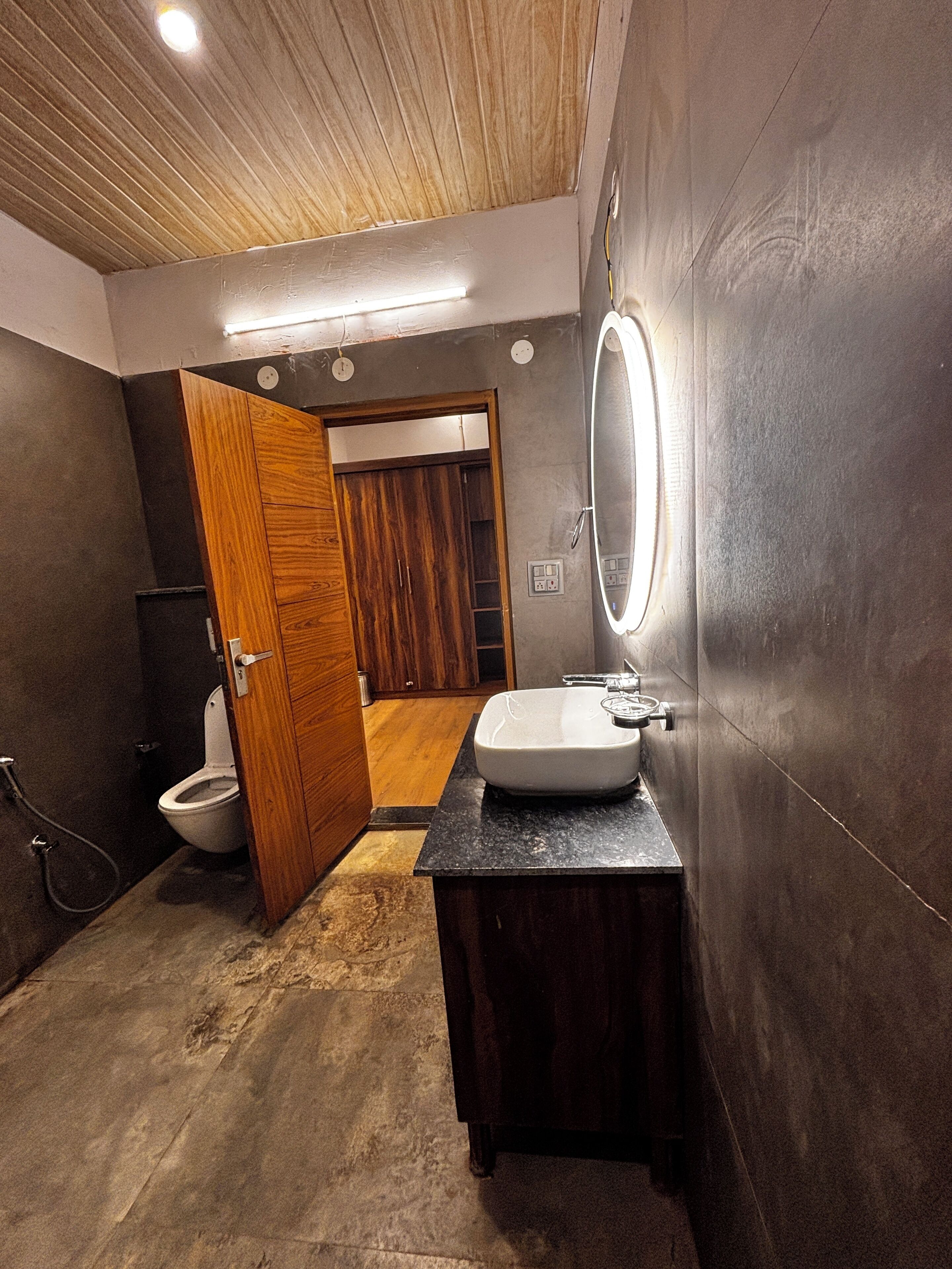A modern bathroom with a wooden door, a white sink, and a mirror.