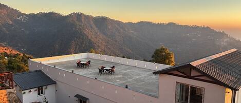 A rooftop terrace with a table and chairs, overlooking a mountainous landscape.