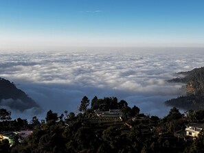 A mountainous landscape with a village nestled among trees, surrounded by clouds. - SERENE FOREST RESORT (Khurpatal)