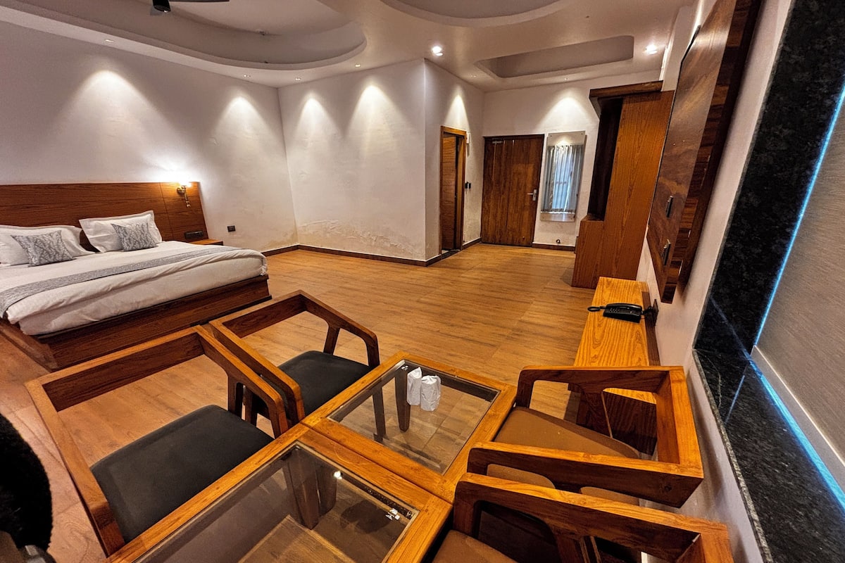 Une chambre d’hôtel moderne, équipée d’un lit, d’une table basse en verre, de chaises en bois et d’un téléviseur fixé au mur.