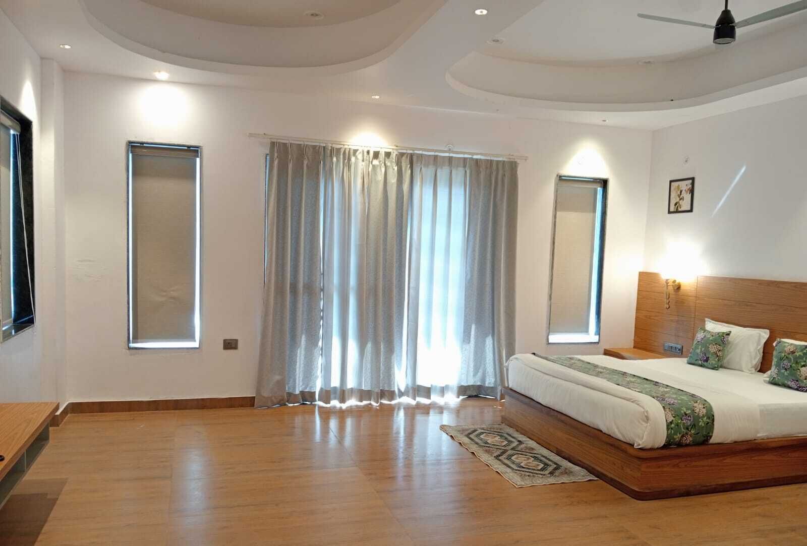 Un dormitorio con suelo de madera, cama con cabecera, ventana con cortinas y ventilador de techo.