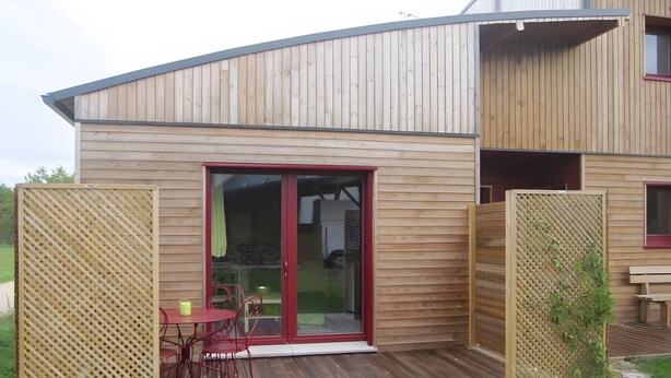 A wooden house with a deck, a sliding glass door, and a red-framed window. - Furnished Cottage in the Land of Castles – Ideal for Cycling (Mont-près-Chambord)