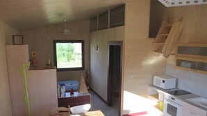 A compact kitchen with a microwave, oven, and wooden cabinets. There is a dining area with a table and chairs, and a window providing natural light. - Furnished Cottage in the Land of Castles – Ideal for Cycling (Mont-près-Chambord)