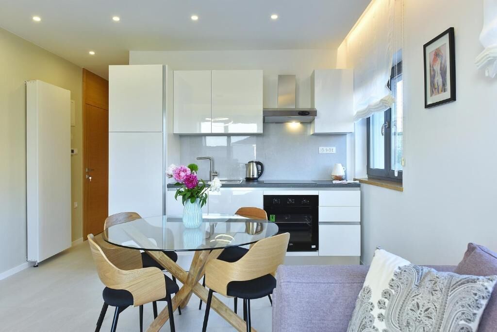 A modern kitchen with white cabinets, a glass dining table, and a coffee machine.