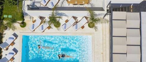 A rooftop swimming pool with lounge chairs and a sunbed area.