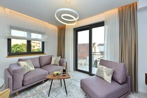 A modern living room with a sofa set, a small table with a bottle and glasses, and a large sliding glass door leading to an outdoor area.