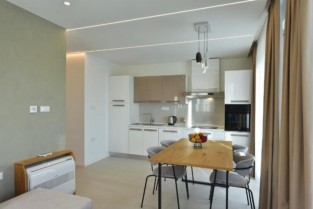A modern kitchen with white cabinets, a wooden dining table, and a fruit bowl.