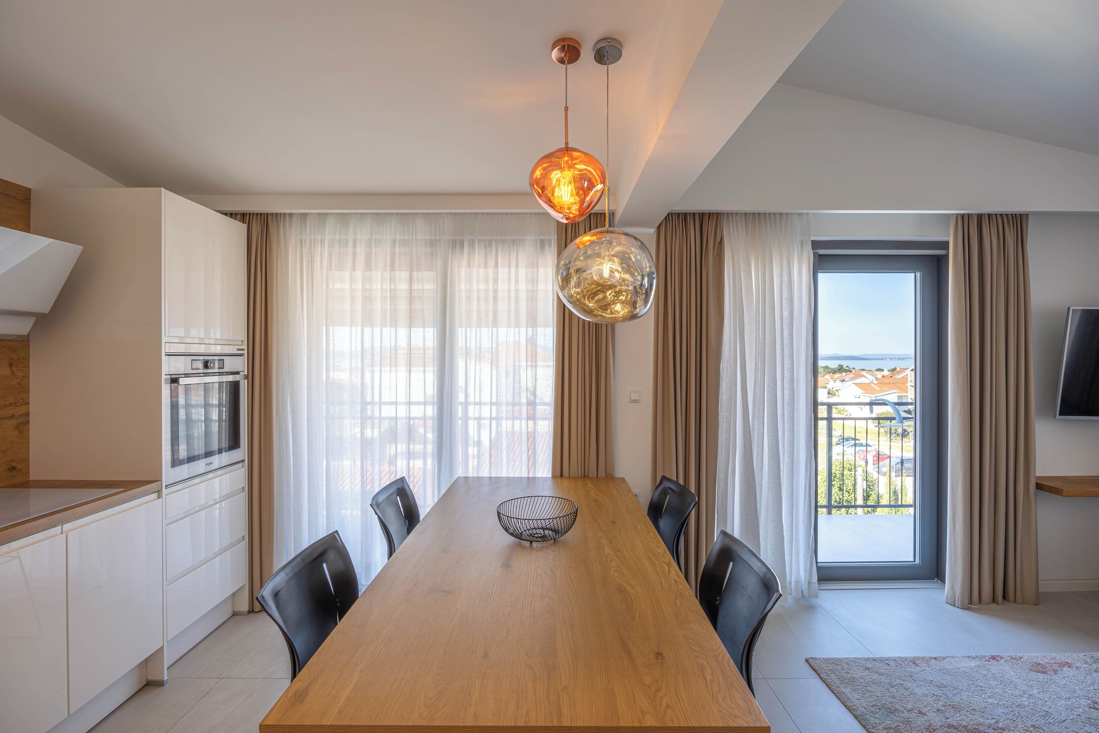 Una cocina moderna con horno integrado, un comedor con mesa y sillas de madera, y un ventanal con vistas.
