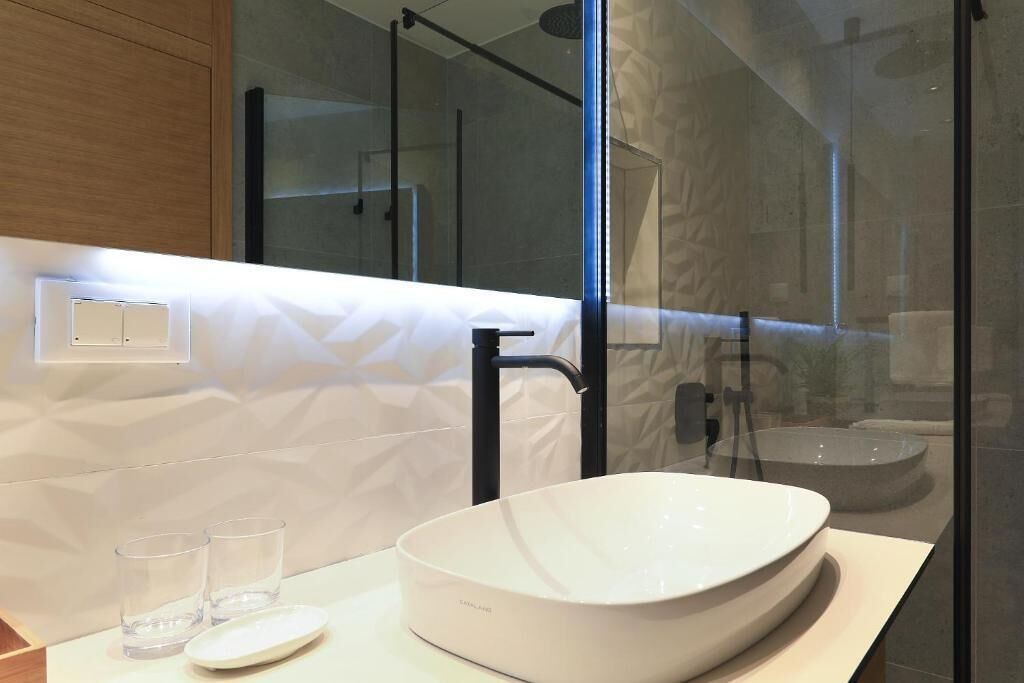 Een moderne badkamer met een groot, wit wasbak, een zwarte kraan en een douchecabine met glazen wanden.