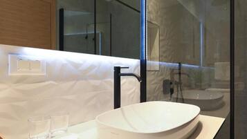 Un baño moderno con un lavamanos blanco de diseño, un grifo negro y una zona de ducha con mampara de vidrio.