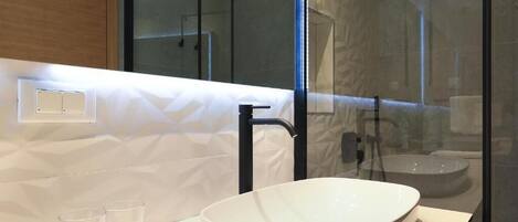 Een moderne badkamer met een groot, wit wasbak, een zwarte kraan en een douchecabine met glazen wanden.