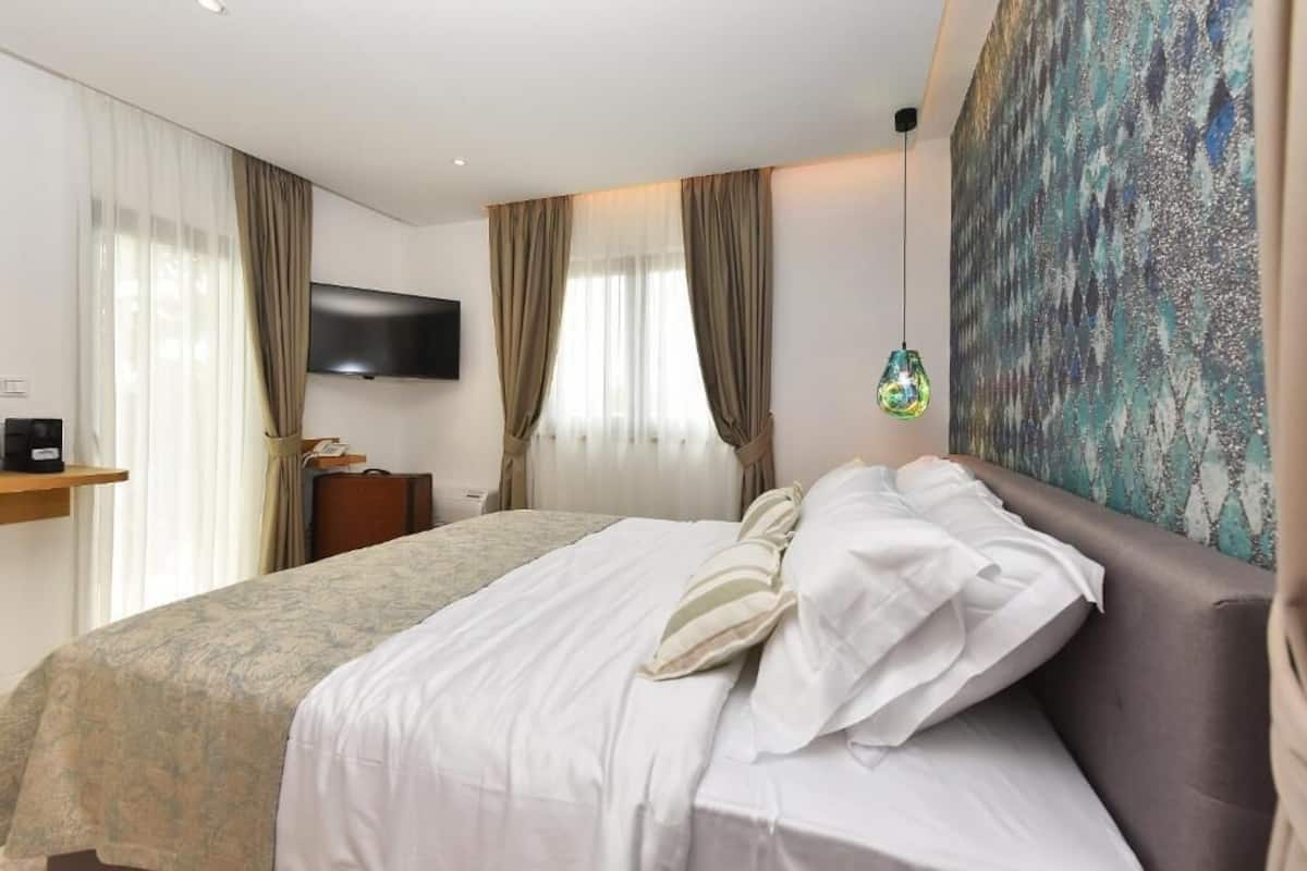 Ein Hotelzimmer mit einem Bett, einem Flachbildfernseher, einem Gemälde und einer Pendelleuchte.