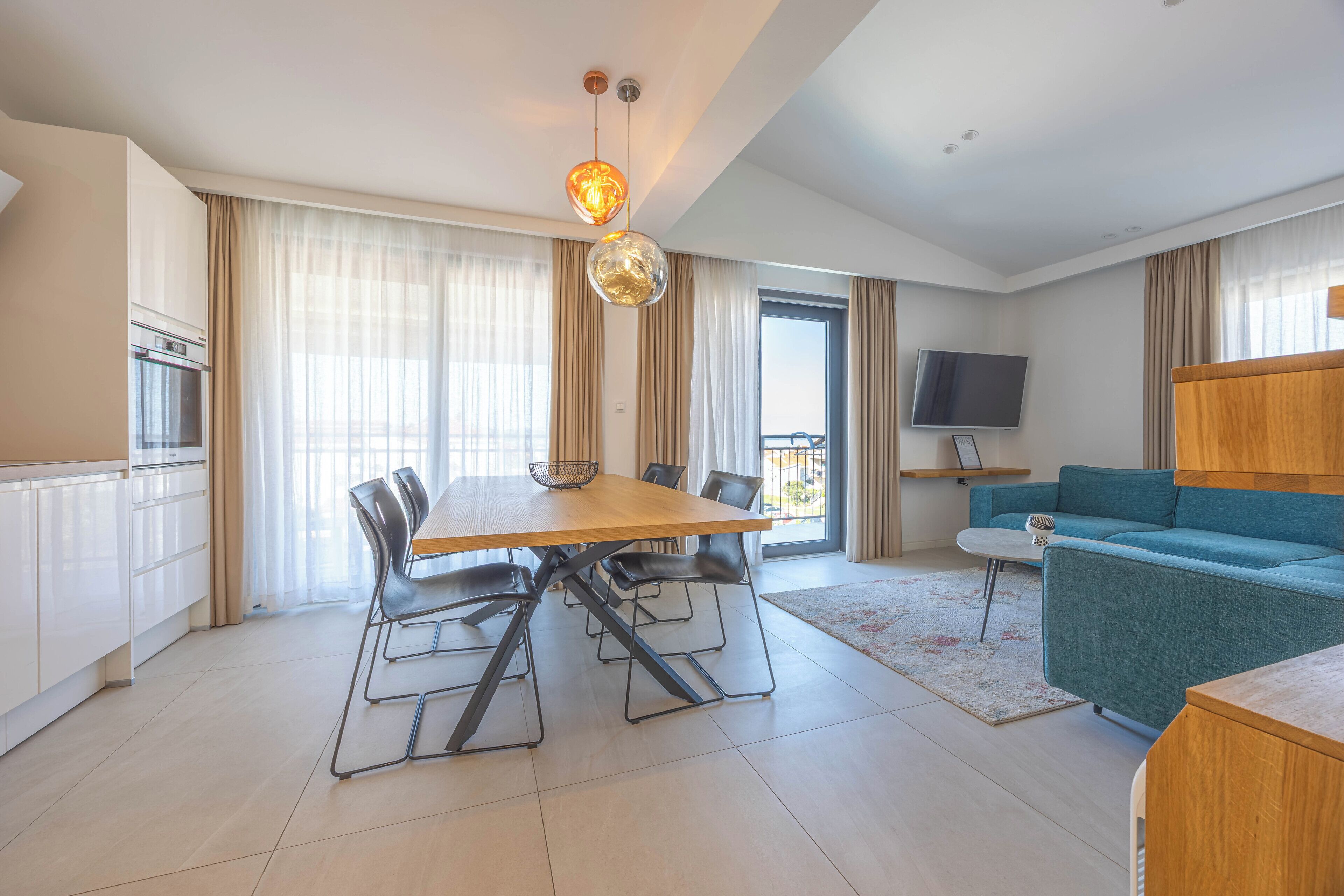 Una sala de estar moderna con una mesa de comedor, sillas, un sofá, un televisor y una zona de cocina con armarios y un microondas.