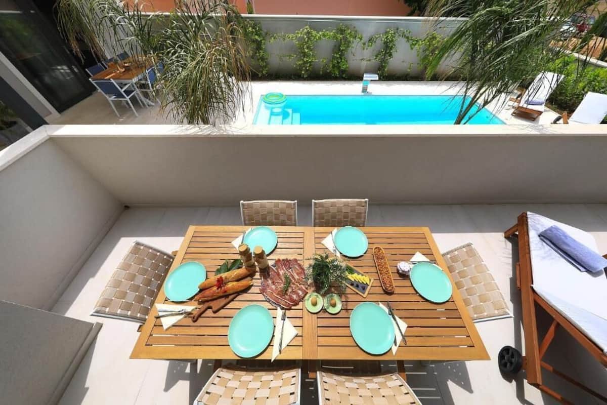 Eine Dachterrasse mit Pool, Esstisch mit Geschirr, Besteck und Speisen, sowie eine Lounge-Liege.