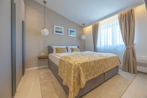 A bedroom with a bed, bedside tables, a wall-mounted shelf, and a window with curtains.