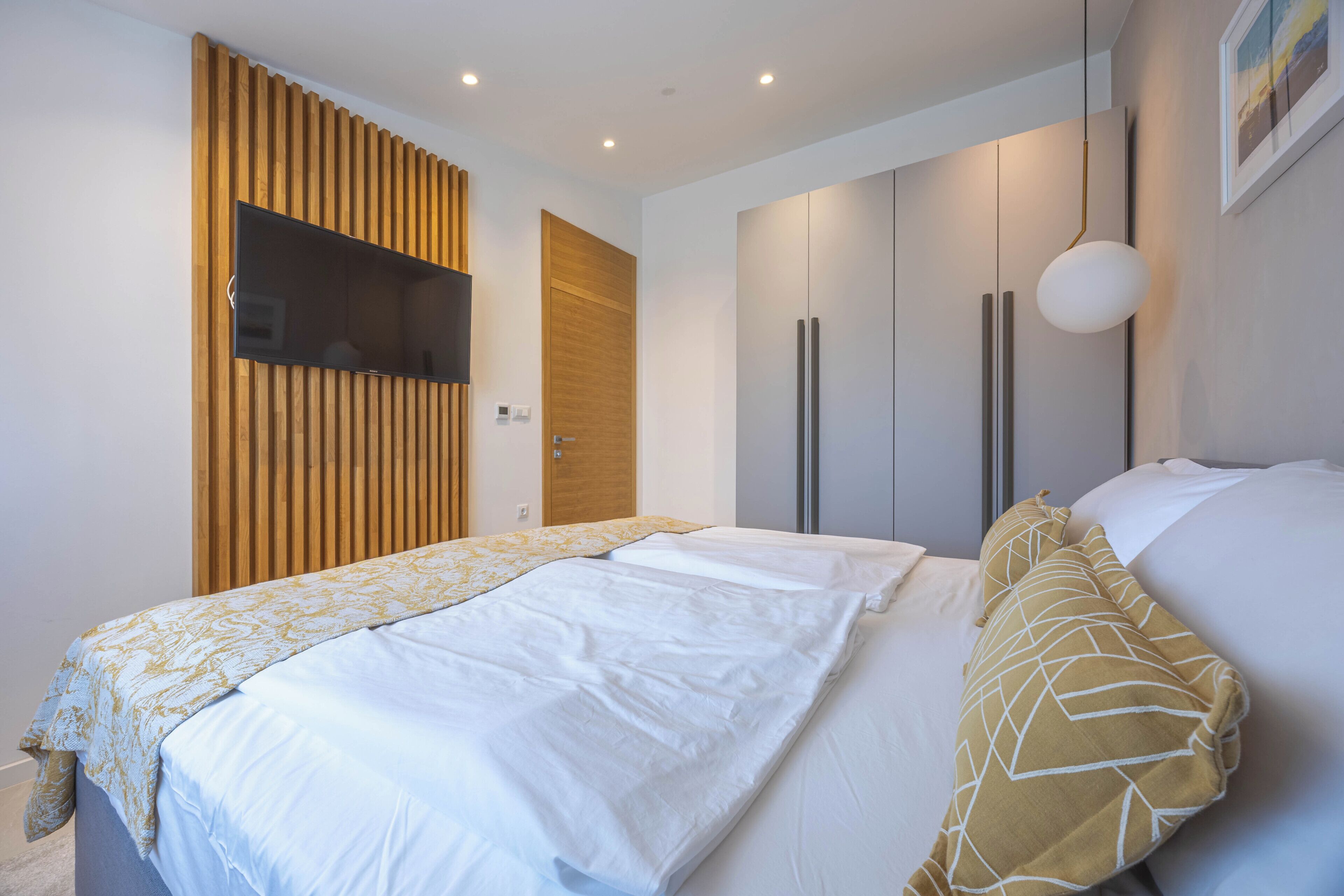 Un dormitorio con una cama, un televisor montado en un panel de madera y un armario.