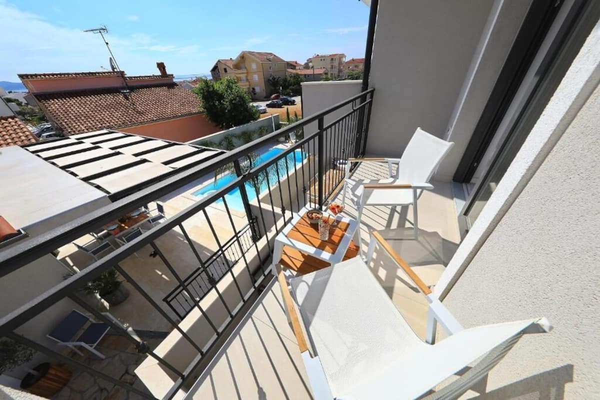 Ein Balkon mit Pool, weißen Liegestühlen und einem Tisch mit einem Getränk.