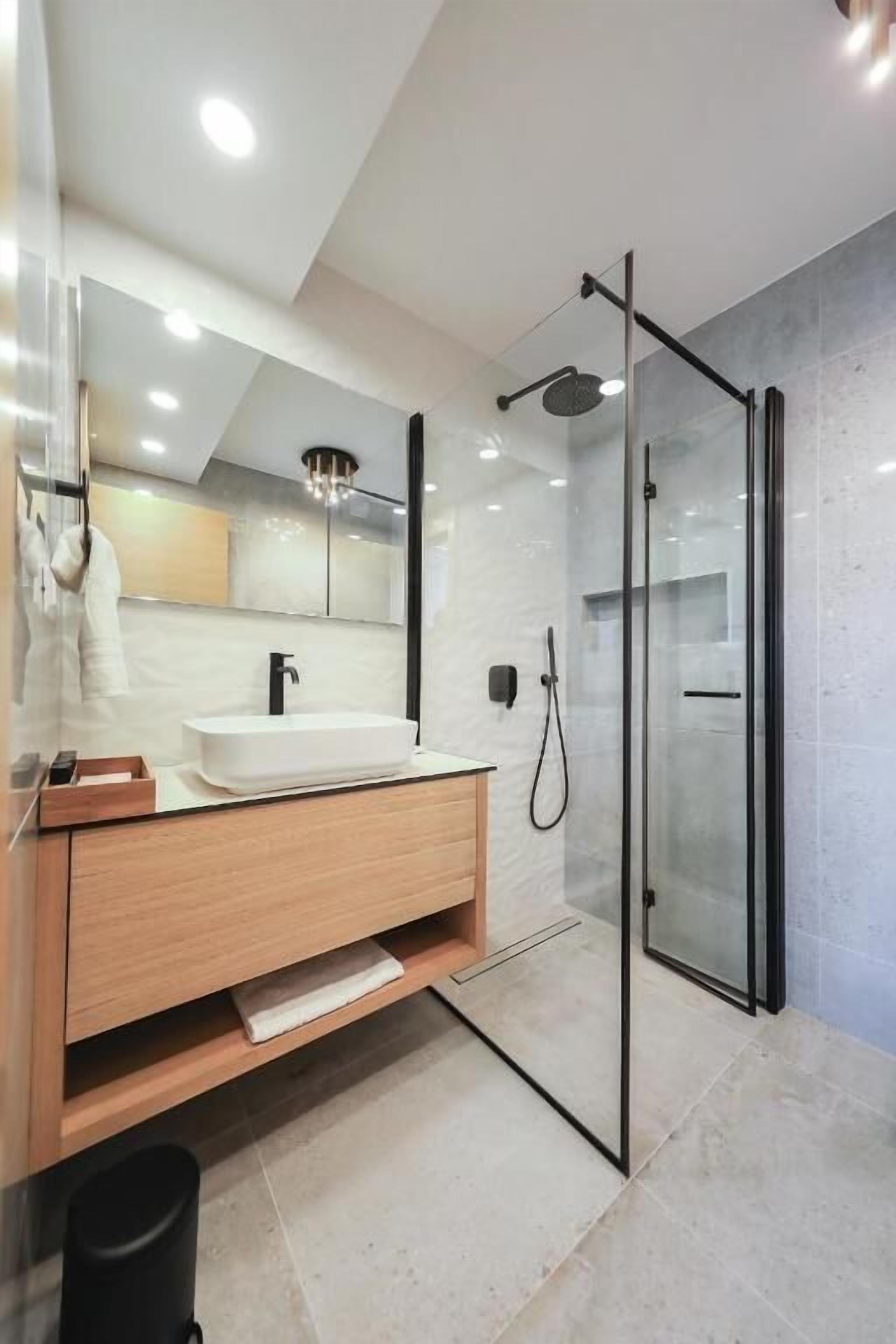 A modern bathroom with a glass-enclosed shower, a wooden vanity, and a large mirror.