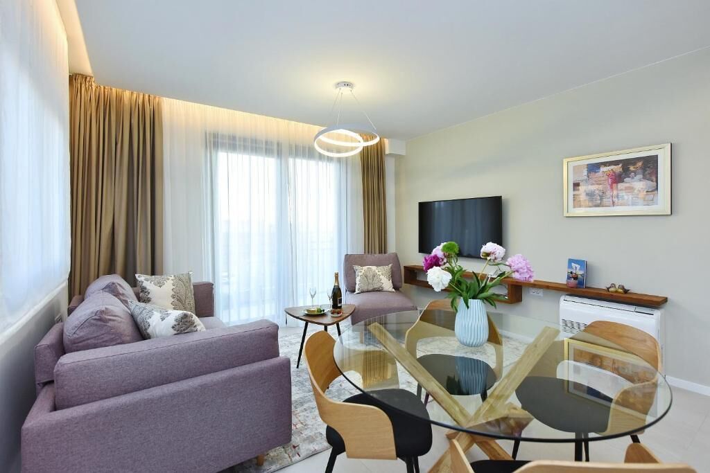 Una sala de estar moderna con un sofá, sillas, una mesa de vidrio para comer, un televisor y un cuadro en la pared.