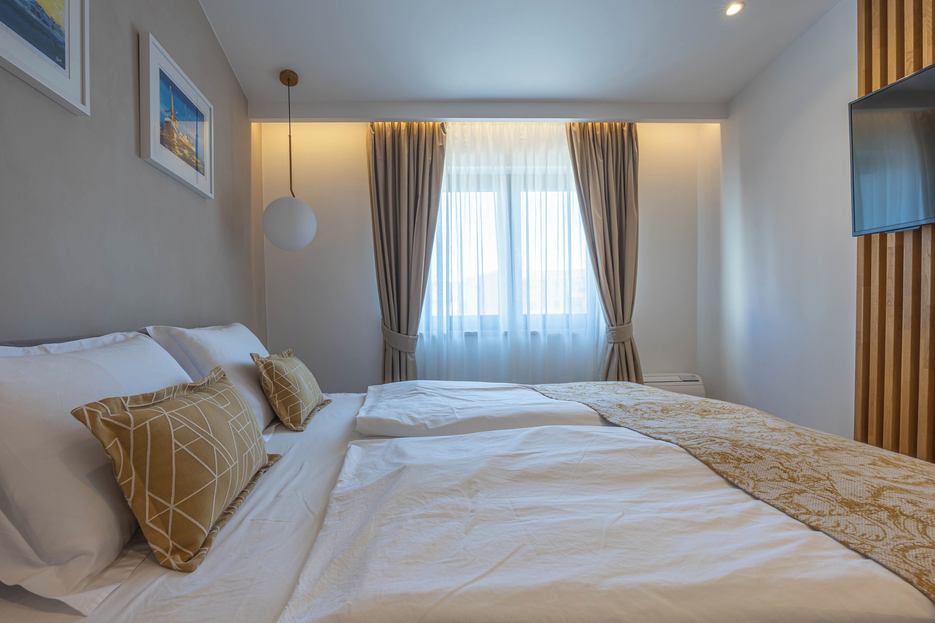 Une chambre d’hôtel avec un lit, deux oreillers, une table de chevet, une télévision et une fenêtre avec des rideaux.
