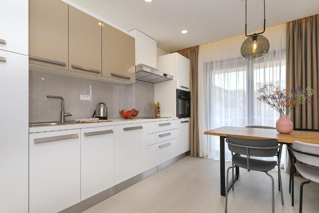 Une cuisine moderne avec des armoires blanches, une hotte en acier inoxydable et un coin repas comprenant une table et des chaises en bois.